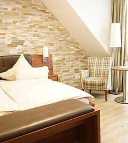 modernes Hotelzimmer mit braunem Bett, beiger Decke, Steinwand und grünen Samtsesseln