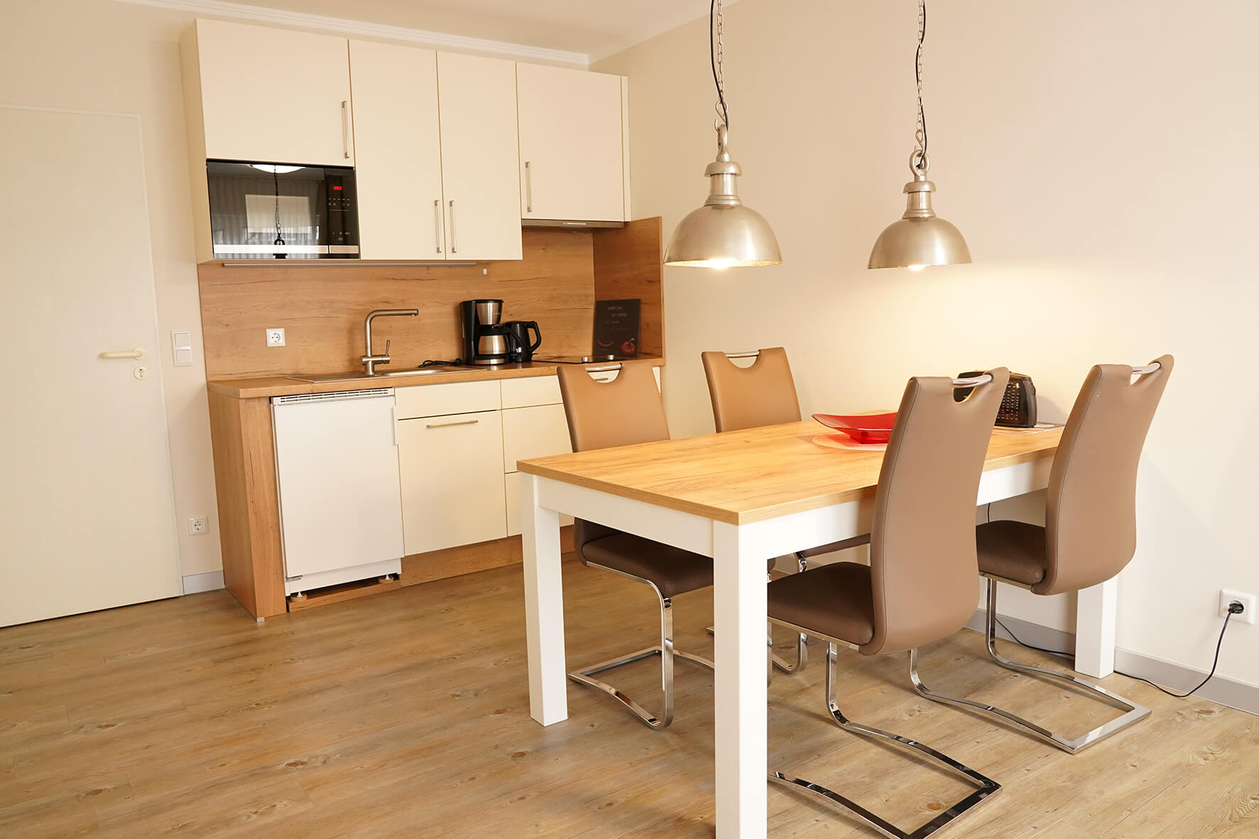Küchenzeile in cremeweiß mit Holztisch und braunen Lederstühlen an einer weißen Wand