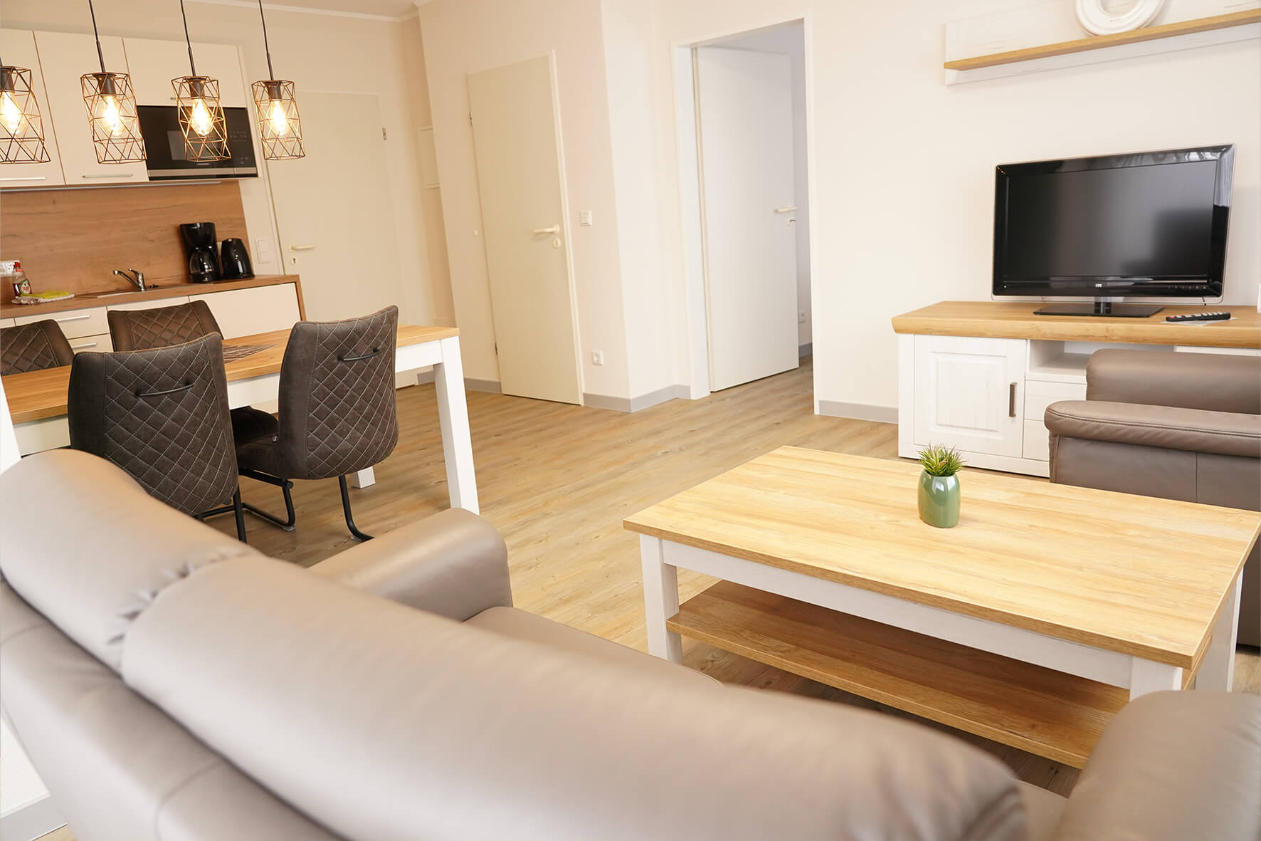 Aufnahme eines Wohnzimmers mit offenem Küchenbereich, Esstisch und Stühlen, braunem fernsehtisch und Flachbildschirmfernseher