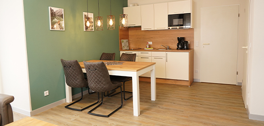 weiße, kleine Küche mit Esstisch und Stühlen an einer waldgrünen Wand