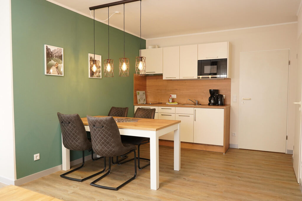 weiße, kleine Küche mit Esstisch und Stühlen an einer waldgrünen Wand