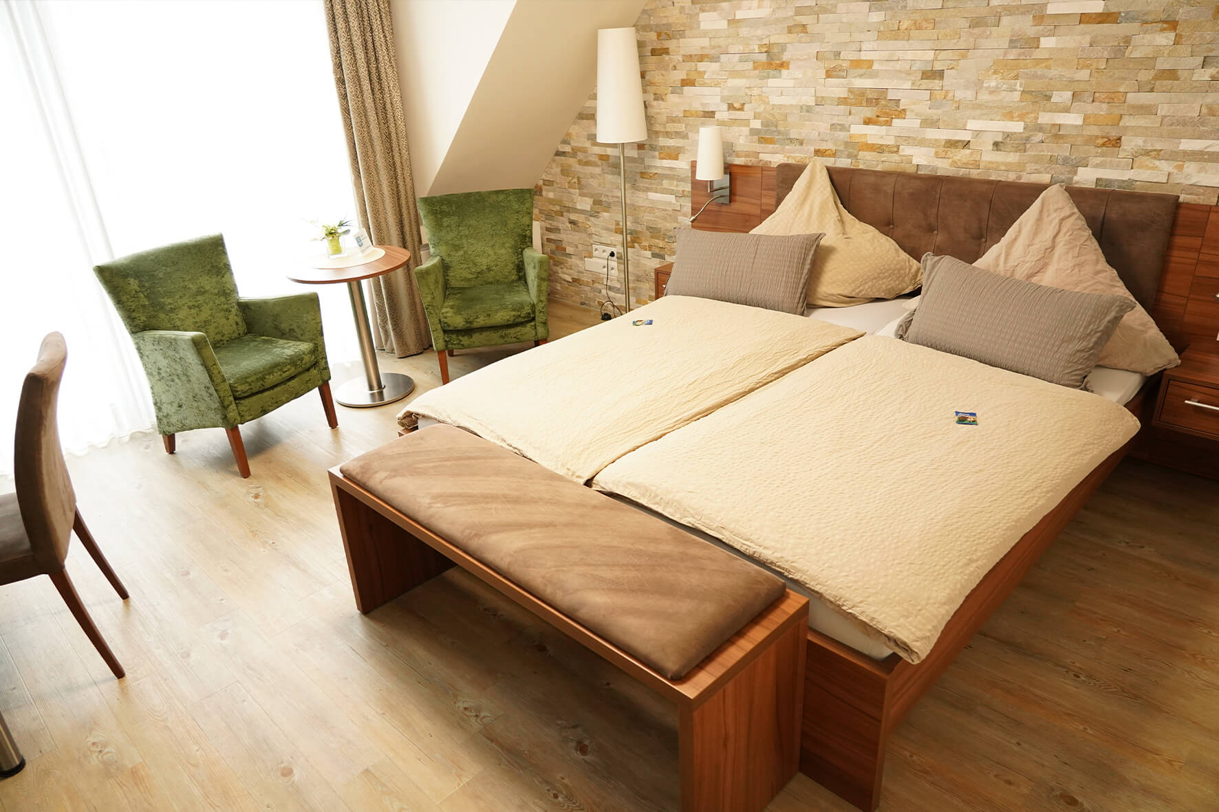 modernes Hotelzimmer mit braunem Bett, beiger Decke, Steinwand und grünen Samtsesseln