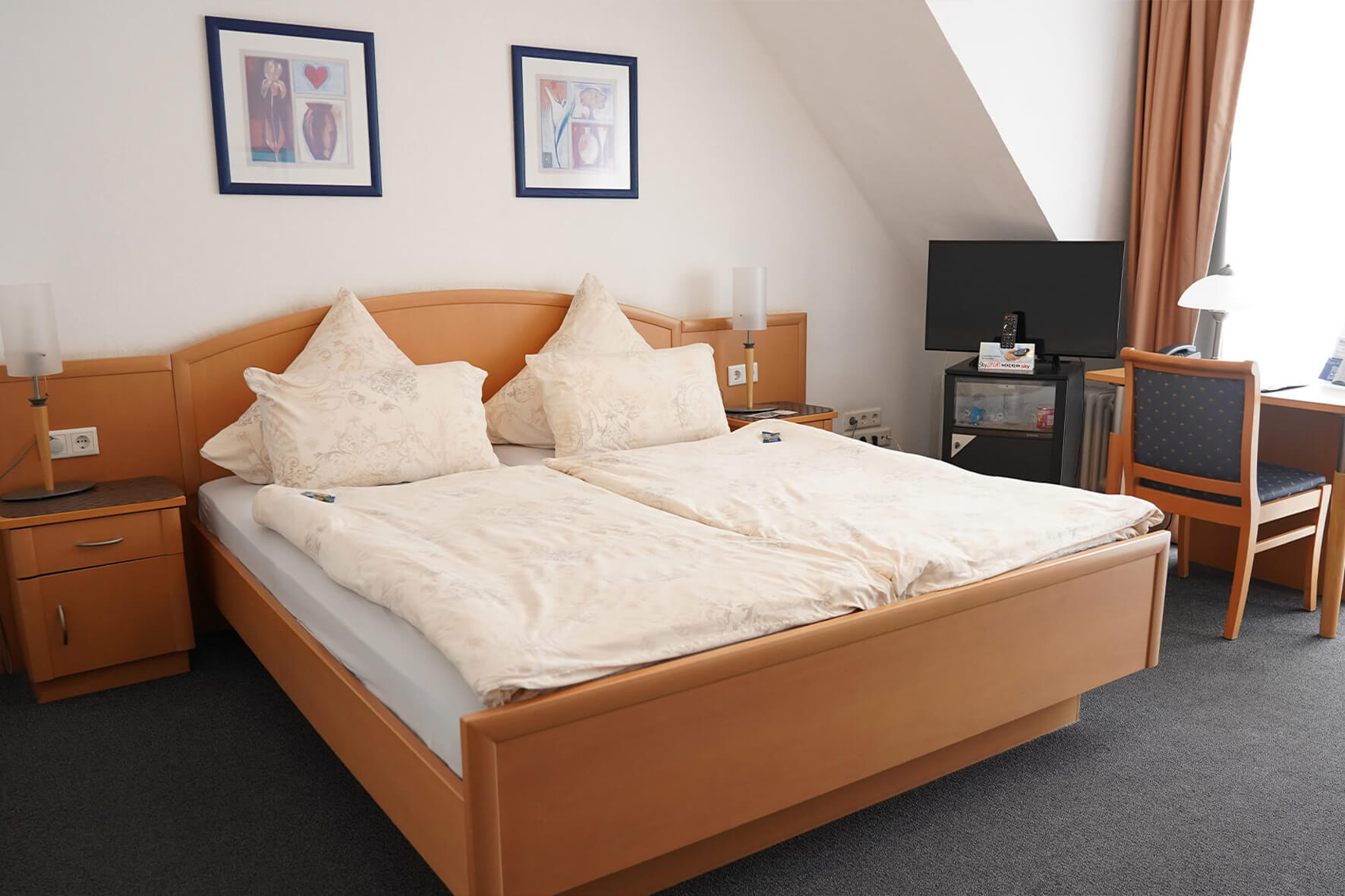 Doppelbett aus Holz in einem Zimmer mit weißen Wänden und dunklen Teppich und einem Flachbildschirmfernseher in der Ecke