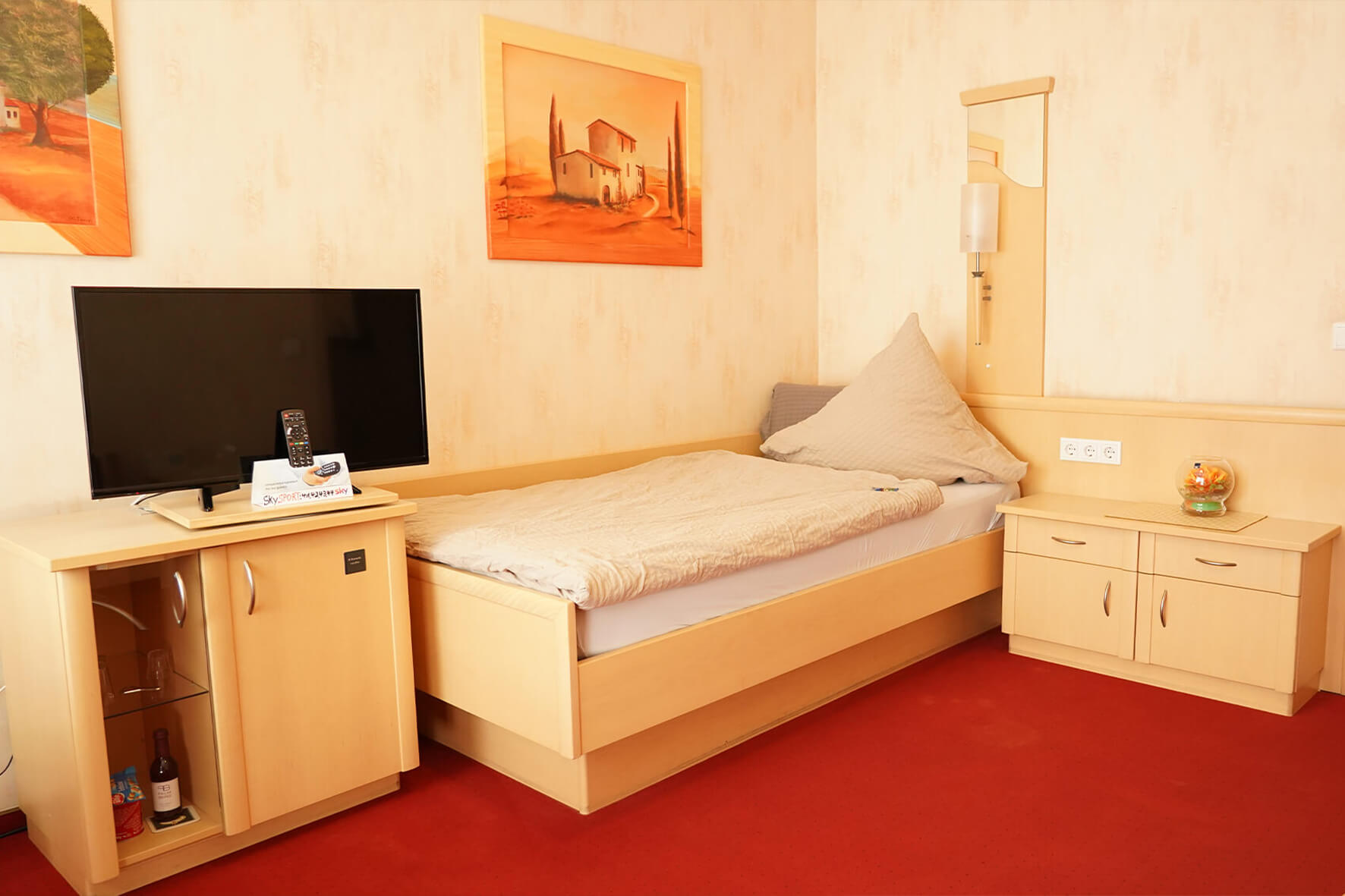 Einzelzimmer mit roten Teppichund heller Holzeinrichtung mit Flachbildschirmfernseher